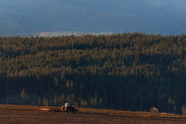 Tractor moving hay field on dark wood and mountain background forest scenery bulgaria rural copy space for text minimal technology agrigulture