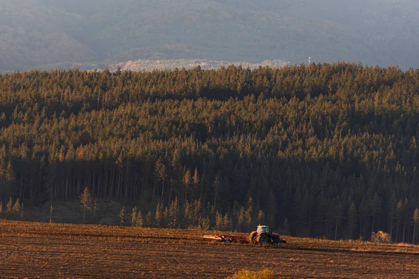 Tractor moving hay field on dark wood and mountain background forest scenery bulgaria rural copy space for text minimal technology agrigulture