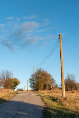 Bulgaristan 'da sonbaharda sakin yamaç yolunun yanındaki eski elektrik hattı direkleri mavi gökyüzü ile Bulgaristan' da canlı altın çimler kırsalında