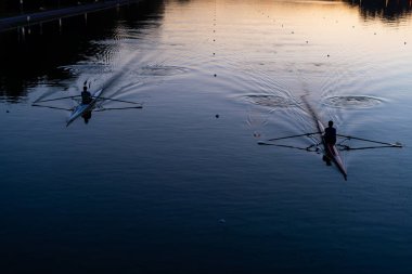 Kanal suyu rezervuarında gün batımında canlı arka planda kürek sporu antrenmanı için yarışan kanolar.