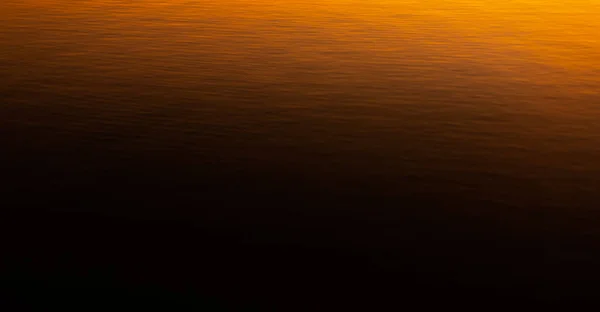 Deep dark orange gradient sunset vibrant reflection in rippled calm water texture