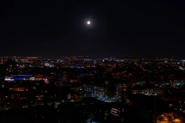 夜には丘の頂上から月明かりと数千もの小さなライトで照らされた大きな暗い街 — ストック写真