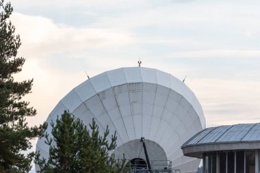 Büyük uydu antenleri yeşil çam ağacı ormanlarında gizlenmiş. Parlak mavi arka planda iletişim merkezi.