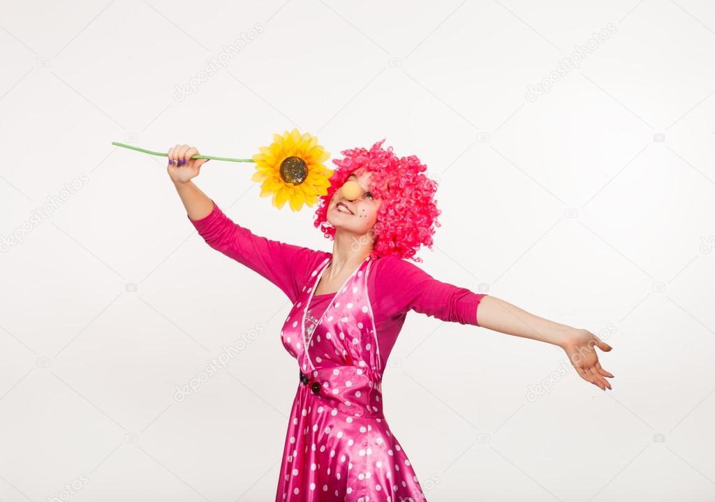 Cheerful, emotional clown in pink wig with yellow flower