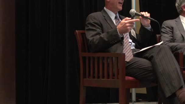 Um profissional sentado com um microfone dando uma palestra — Vídeo de Stock
