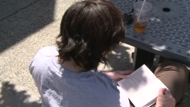 Un joven leyendo en una mesa a lo largo de la acera — Vídeo de stock