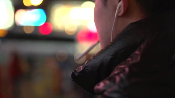 Молодой человек с наушниками курит сигарету — стоковое видео