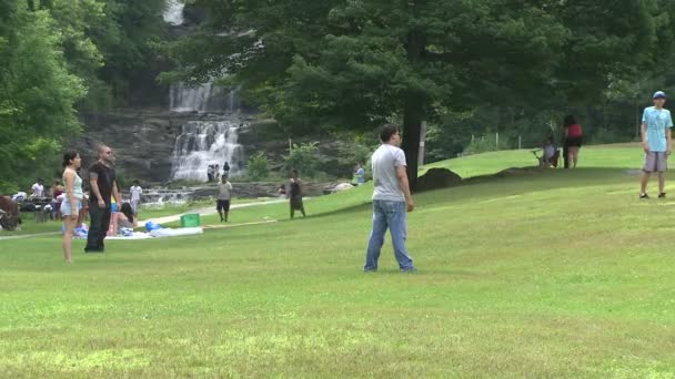 Молоді люди, які грають у м'яч в парку з водоспадом на тлі (4 з 4) — стокове відео