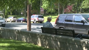 Park edilmiş araba önünde kaldırım bankta oturan adam
