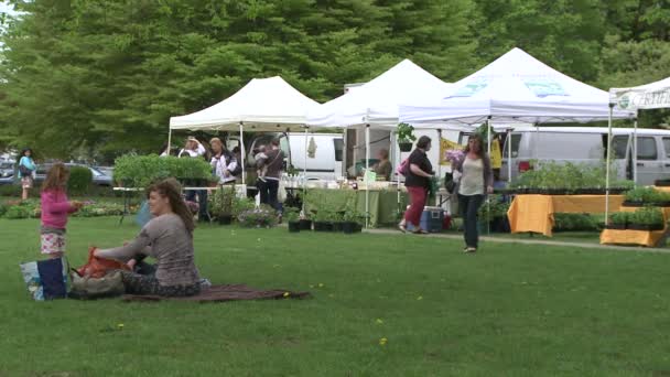 Famille assise sur une couverture dans l'herbe devant une foire aux plantes — Video