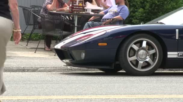 Спортивный автомобиль, сидящий перед людьми, которые едят в маленьком кафе на тротуаре — стоковое видео