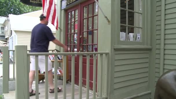 Un hombre entrando en una pequeña tienda con una bandera americana colgando en el frente — Vídeo de stock