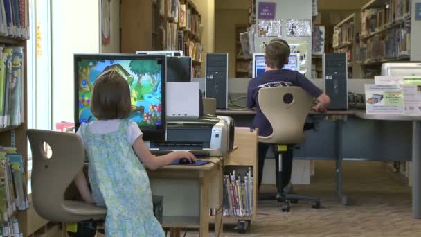 Двое детей пользуются компьютерами в библиотеке — стоковое видео