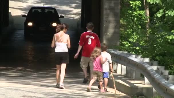 Une randonnée en famille sous un petit pont avec une voiture qui passe — Video