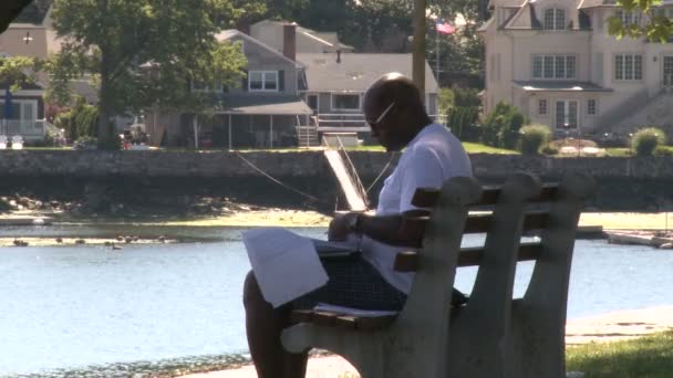 Muž sedí na lavičce s výhledem na vodu, třídění dokumentů. (část 1 ze 2) — Stock video