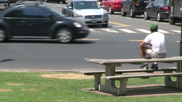 Um homem sentado em um banco de piquenique observando o tráfego . — Vídeo de Stock