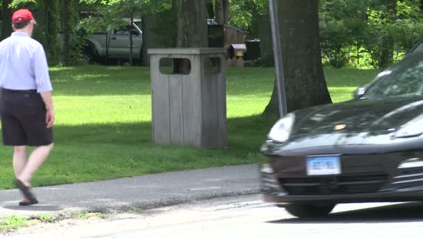 Pessoas andando pela calçada por um dispensador de lixo ao longo da borda de um parque — Vídeo de Stock