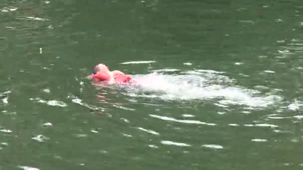 En pojke som simmar i floden med flytväst på — Stockvideo