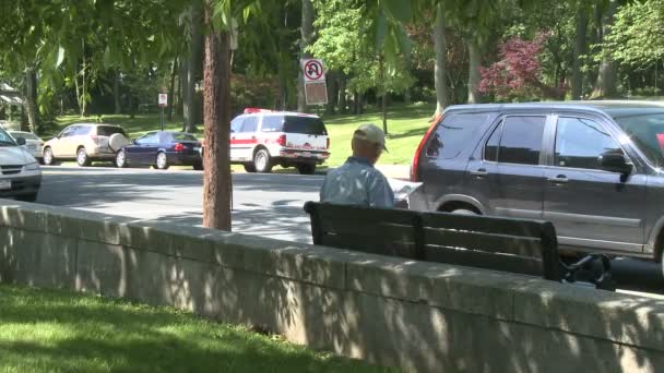 Park edilmiş araba önünde kaldırım bankta oturan adam — Stok video