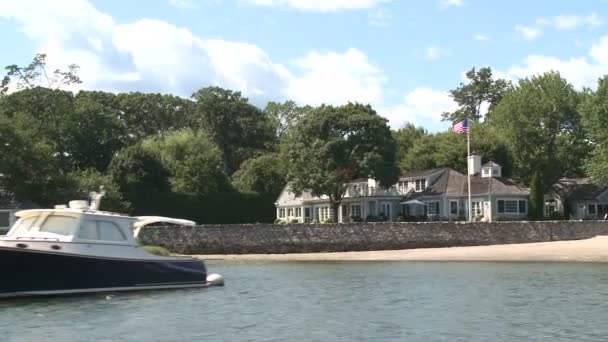 Ett stort hem på vattnet, med en båt förtöjd ute. — Stockvideo