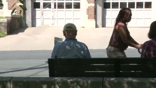 Dos personas sentadas en un banco frente a una vieja estación de bomberos — Vídeo de stock