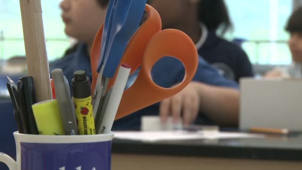 Una taza con bolígrafos, una regla y tijeras con estudiantes en el fondo (1 de 2 ) — Vídeo de stock