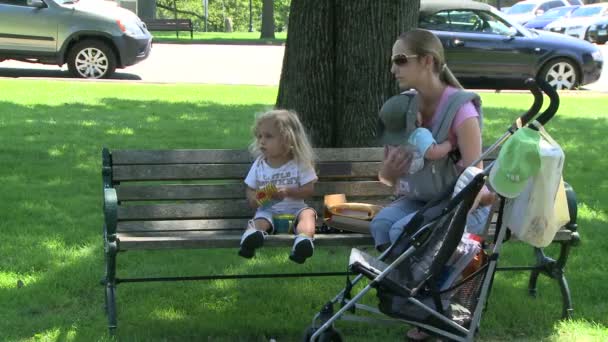 Mère avec bébé et tout-petit assis sur le banc du parc — Video