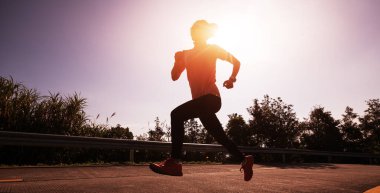 Kadın koşucu kış günü güneşin doğuşunda dağın tepesinde koşuyor.