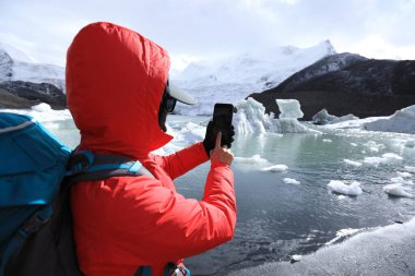 Kadın yürüyüşçü kışın akıllı telefonuyla buzulun fotoğrafını çekiyor.