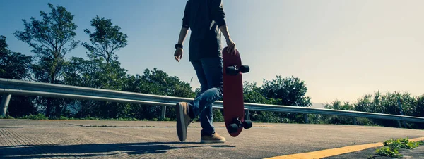 Skateboarder with skateboard walking on sunrise mountain peak