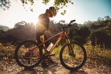 Bisikletçi kadın, gündoğumu kış ormanı patikasındaki bisiklet yüksekliğini ayarlıyor.
