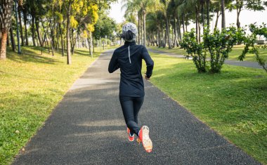 Güneşli tropikal park parkında maraton antrenmanı için koşan kadın.