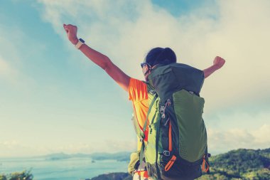 Sahildeki dağın tepesinde kollarını açmış doğanın tadını çıkaran neşeli bir kadın.