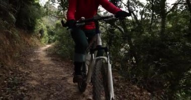 Kırmızı sırt çantalı bisikletli bir kadın ormanda bisiklete biniyor.