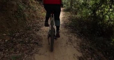 Kırmızı sırt çantalı bisikletli bir kadın ormanda bisiklete biniyor.