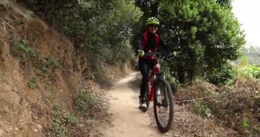 Kırmızı sırt çantalı bisikletli bir kadın ormanda bisiklete biniyor.