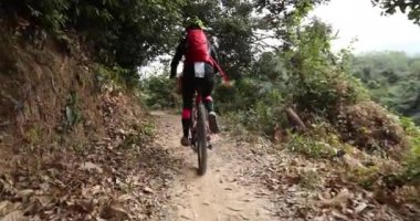 Kırmızı sırt çantalı bisikletli bir kadın ormanda bisiklete biniyor.