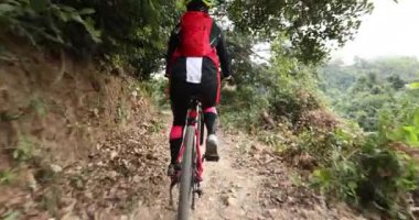 Kırmızı sırt çantalı bisikletli bir kadın ormanda bisiklete biniyor.