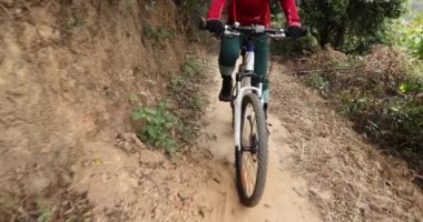 Kırmızı sırt çantalı bisikletli bir kadın ormanda bisiklete biniyor.