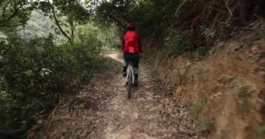 Kırmızı sırt çantalı bisikletli bir kadın ormanda bisiklete biniyor.