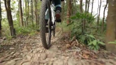 Kırmızı sırt çantalı bisikletli bir kadın ormanda bisiklete biniyor.