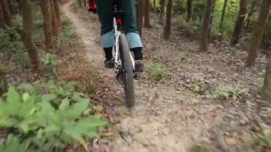 Kırmızı sırt çantalı bisikletli bir kadın ormanda bisiklete biniyor.