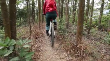 Kırmızı sırt çantalı bisikletli bir kadın ormanda bisiklete biniyor.