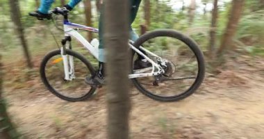 Kırmızı sırt çantalı bisikletli bir kadın ormanda bisiklete biniyor.