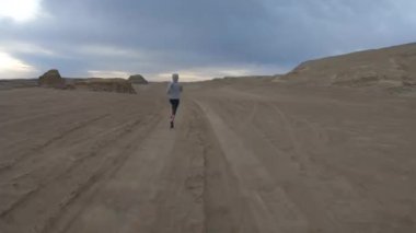 Çöl kum tepelerinde koşan genç bir kadın.