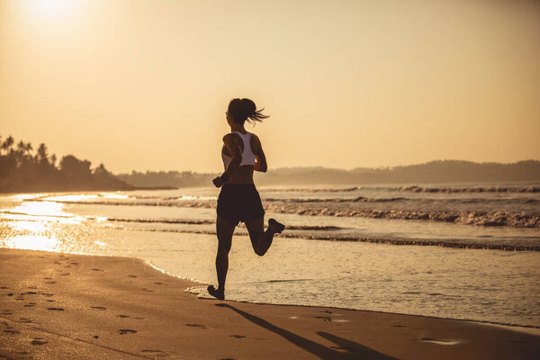 Young fitness woman running at sunrise beach 