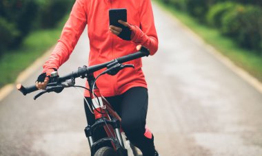 Bisikletçi orman yolunda dağ bisikleti sürerken akıllı telefon kullanır