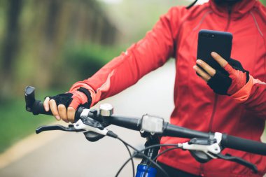 Bisikletçi orman yolunda dağ bisikleti sürerken akıllı telefon kullanır