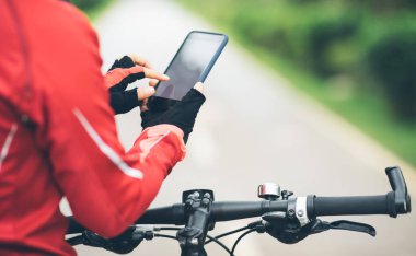 Bisikletçi orman yolunda dağ bisikleti sürerken akıllı telefon kullanır