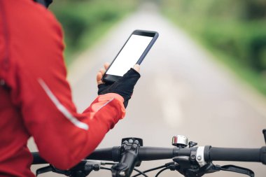 Bisikletçi orman yolunda dağ bisikleti sürerken akıllı telefon kullanır